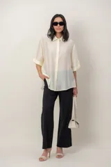 Camisa de seda de corte oversize y color marfil, con cuello camisero, cierre frontal de botones y mangas cortas con vuelta.