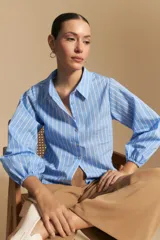 Camisa azul a rayas blancas, de manga larga con puños elastizados, entallada en la cintura y con cierre de botones frontales.