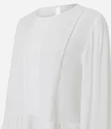 Blusa tipo bata de color blanco, confeccionada en viscosa, con cuello redondo, mangas largas con puños abotonados, detalles de entremedios verticales y un recorte con volado en el bajo.