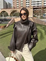 Chaqueta de efecto cuero con cuello alto, cierre frontal cruzado con botones a presión, hombreras y cintura elástica. Presenta un acabado texturizado y bolsillos laterales.