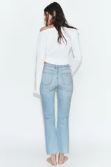 Jeans de tiro alto con diseño cropped flare, confeccionados en denim azul con acabado desgastado. Presentan cinco bolsillos, cierre frontal con cremallera y botón metálico, y bajo con terminación sin costuras.