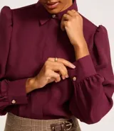 Camisa celeste de crepé con cuello inglés, manga larga abullonada y abotonadura frontal.