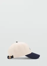 Gorra Archive de color beige con visera y botón superior azul marino. Cuenta con mensaje bordado en el lateral y cierre regulable con hebilla metálica.