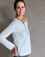 Remera blanca de manga larga con cuello en V y costuras decorativas en contraste. Incluye un lazo ajustable en el cuello con herraje metálico circular.