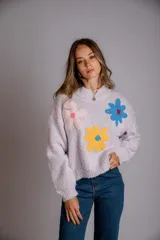 Buzo de tejido de punto grueso, color lila claro, con cuello redondo y apliques de flores tejidas en tonos rosa pálido, amarillo y azul.