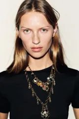 Pack de dos collares de eslabones metálicos labrados en tono dorado envejecido. El collar más largo presenta un dije colgante principal con forma de flor negra y detalles dorados, además de pequeños dijes colgantes. El collar más corto tiene múltiples dijes colgantes que incluyen un corazón amarillo, una piedra rosada, un dije ovalado negro con flores doradas, un dije redondo con flor roja, un dije cuadrado con mariposa negra, y otros dijes pequeños como una perla y un dije negro ovalado.