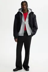Campera con capucha de felpa gris, con cierre frontal completo, bolsillos tipo canguro y estampado tipográfico en el pecho. Presenta hombros caídos y puños acanalados.