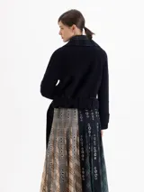Chaqueta de lana azul marino con solapas en contraste a cuadros, cierre frontal con botones y detalles de ganchos metálicos decorativos. Incluye cinturón de tela con hebilla metálica para ajustar la cintura.