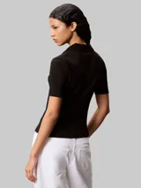 Chomba de Calvin Klein confeccionada en tejido canalé de algodón con elastano. Presenta cuello tipo polo con cartera de dos botones, mangas cortas y un ajuste estructurado. Incluye una pequeña insignia de la marca en el dobladillo inferior.