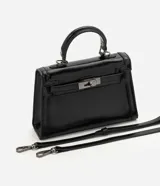 Cartera bandolera Satinato pequeña, de estructura rígida y diseño rectangular, confeccionada en PU negro con acabado levemente brillante. Cuenta con cierre frontal metálico con traba, asa de mano superior y correa larga removible y ajustable.