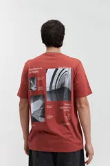 Remera de manga corta color terracota con estampado frontal blanco que dice "MISTRAL Architecture of Reality REG. TM / EST. 76". Tiene un fit regular y está confeccionada en algodón.