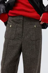 Pantalón de tiro alto en color marrón oscuro, con diseño de pierna recta y pliegues frontales cosidos. Presenta bolsillos de parche delanteros con botones decorativos dorados.