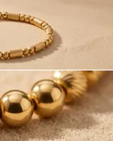 Pulsera tipo esclava rígida de acero con baño de oro, con diseño de eslabones texturizados y esferas lisas intercaladas.