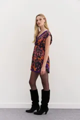 Vestido corto con escote en V y espalda semidescubierta. Presenta un estampado abstracto en tonos naranja, negro y violeta, con bordes a contratono en color violeta en el escote y el ruedo. Cuenta con cintura elástica y frunces en los hombros.