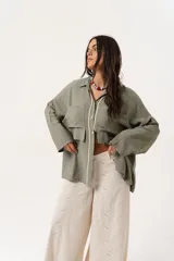 Camisa verde militar de manga larga con silueta oversize, dos bolsillos delanteros y corte levemente más largo en la espalda. Escote en V abotonado con detalle de galón picot a lo largo de la cartera y botones a tono. Isotipo bordado en la parte trasera.