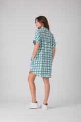 Vestido camisero de corte holgado y silueta relajada, con cuello clásico, cierre frontal de botones y mangas cortas con dobladillo. Presenta un estampado de cuadros irregulares en color bordó sobre fondo blanco.