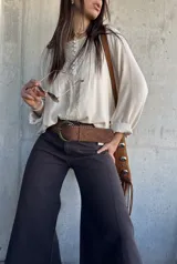 Blusa beige de corte oversize, con mangas largas, botones forrados en el frente y detalles de puntillas y alforzas verticales.