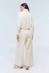 Pantalón de vestir color crema, de corte ancho y tiro alto. Se ajusta a la cintura con cinturón de cuero marrón.