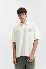 Remera polo color crema con logo bordado en el pecho, de corte amplio y mangas cortas.