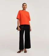 Blusa básica de mujer color negro, confeccionada en malla encorpada de algodón, con cuello redondo y mangas cortas de corte oversized con sisas desplazadas.