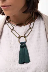 Collar de cadena con eslabones rectangulares en tono bronce, diseñado para ser versátil y usarse largo o doble. Presenta un dije central en forma de herradura del cual cuelgan tres borlas de hilo en color verde oscuro.