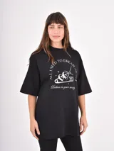 Remera negra de corte oversize con cuello redondo y mangas cortas. Presenta un estampado gráfico en el frente con un imperdible, una estrella y la frase 'All I need to dream about' junto a 'Belive in your magic'.