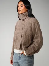 Chaqueta corta de corte recto con estampado de cuadros pequeños en tonos marrones y beige. Presenta cuello alto, mangas largas y cierre frontal oculto.