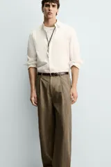 Pantalón de corte relajado confeccionado en mezcla de algodón y lino, con diseño de pliegues frontales, bolsillos laterales y bolsillos traseros de vivo. Presenta cierre frontal con cremallera y botón, con un acabado de lavado especial que le otorga una apariencia única.