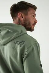 Buzo canguro de felpa color verde militar con estampado en la espalda con el logo de la marca Brookfield. Tiene capucha con cordones ajustables y bolsillo canguro.