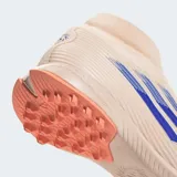 Championes de fútbol Adidas F50 Sparkfusion League, diseñados para mujer. El calzado es de caña media con cuello tejido, exterior en tono beige claro con franjas azules y detalles en naranja coral en la suela.