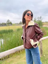 Campera de cuero de oveja italiano con diseño slouchy, cuello de piel sintética desmontable y detalles de piel en puños y bolsillos. Presenta cierre frontal con botones a presión.