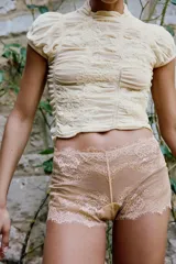 Top de punto con mezcla de viscosa, color beige, con cuello subido y manga corta. Presenta un diseño con frunces verticales y detalles bordados a tono, con terminación de ruedo ondulado.