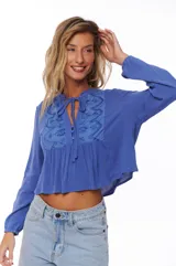 Blusa azul con escote en V y lazos, mangas largas y detalles bordados en el pecho.