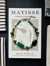 Collar corto de cuentas con dijes en tonos verdes, blanco y negro, con cierre ajustable de cadena metálica.