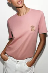 Camiseta de algodón con efecto lavado, cuello redondo y manga corta. Presenta un detalle de fornitura metálica aplicada en el pecho.