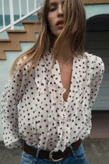 Blusa de escote en pico con volantes frontales, manga larga con puños elásticos y cierre frontal con botones.