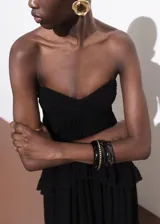 Vestido largo de fiesta color negro, con escote palabra de honor y diseño evasé. Presenta múltiples niveles con volantes decorativos y cierre lateral con cremallera.