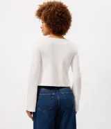 Blusa de algodón con cuello bote y mangas largas. Presenta un diseño asimétrico en el bajo decorado con un delicado detalle de encaje.