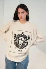 Sweater de punto oversize color crudo, con cuello redondo y diseño bordado a mano en el frente representando al signo Cáncer con un cangrejo, un corazón y una estrella.