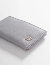 Billetera de cuero vegano color verde claro, con cierre superior y aplique metálico con logo en la parte frontal.