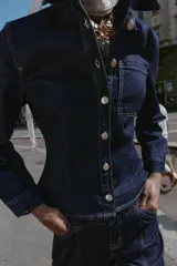 Camisa de denim color azul oscuro, de manga larga y corte entallado. Presenta cuello solapa, un bolsillo de plastrón en el pecho y cierre frontal con botones dorados.