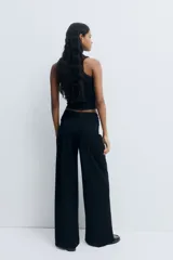 Pantalón de tiro alto negro, de corte holgado y pernera recta, confeccionado en punto grueso. Presenta un diseño drapeado con un detalle de nudo o giro en la parte frontal de la cintura.