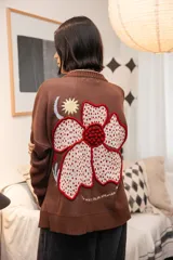 Saco tejido color chocolate con diseño inspirado en la granada, con flores y soles bordados. Presenta cierre frontal con botones, cuello redondo y puños acanalados.