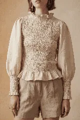 Blusa color verde oliva confeccionada en muselina de algodón, con cuello alto con volados, mangas largas abullonadas y elástico en puños, delantera y espalda. Cierre con botón forrado en la espalda.