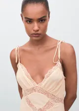 Vestido midi de estilo lencero en color crema, con escote en pico y detalles de encaje en el pecho y la cintura. Presenta tirantes finos ajustables y un diseño evasé con caída fluida.