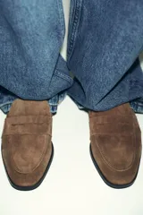 Mocasín plano de mujer confeccionado en serraje, con diseño de antifaz en el empeine, costuras visibles y punta redonda.