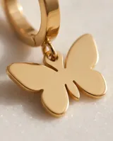 Par de caravanas tipo argolla en acero dorado, con un dije colgante en forma de mariposa minimalista.