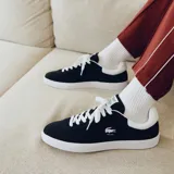 Championes Lacoste modelo Baseshot, de diseño urbano y perfil bajo. Confeccionados en gamuza color azul marino, presentan cordones blancos, suela de goma blanca y el logo del cocodrilo bordado en el lateral con la inscripción EST. 1933.
