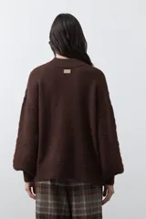 Sweater de punto color marrón chocolate, con cuello redondo, mangas largas abullonadas y puños ajustados. Presenta un diseño de textura acanalada horizontal y silueta relajada.