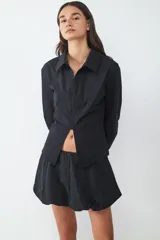 Camisa de manga larga con cuello clásico, confeccionada en popelín. Presenta un cierre frontal con cremallera y una abertura en el bajo que deja ver la cintura.